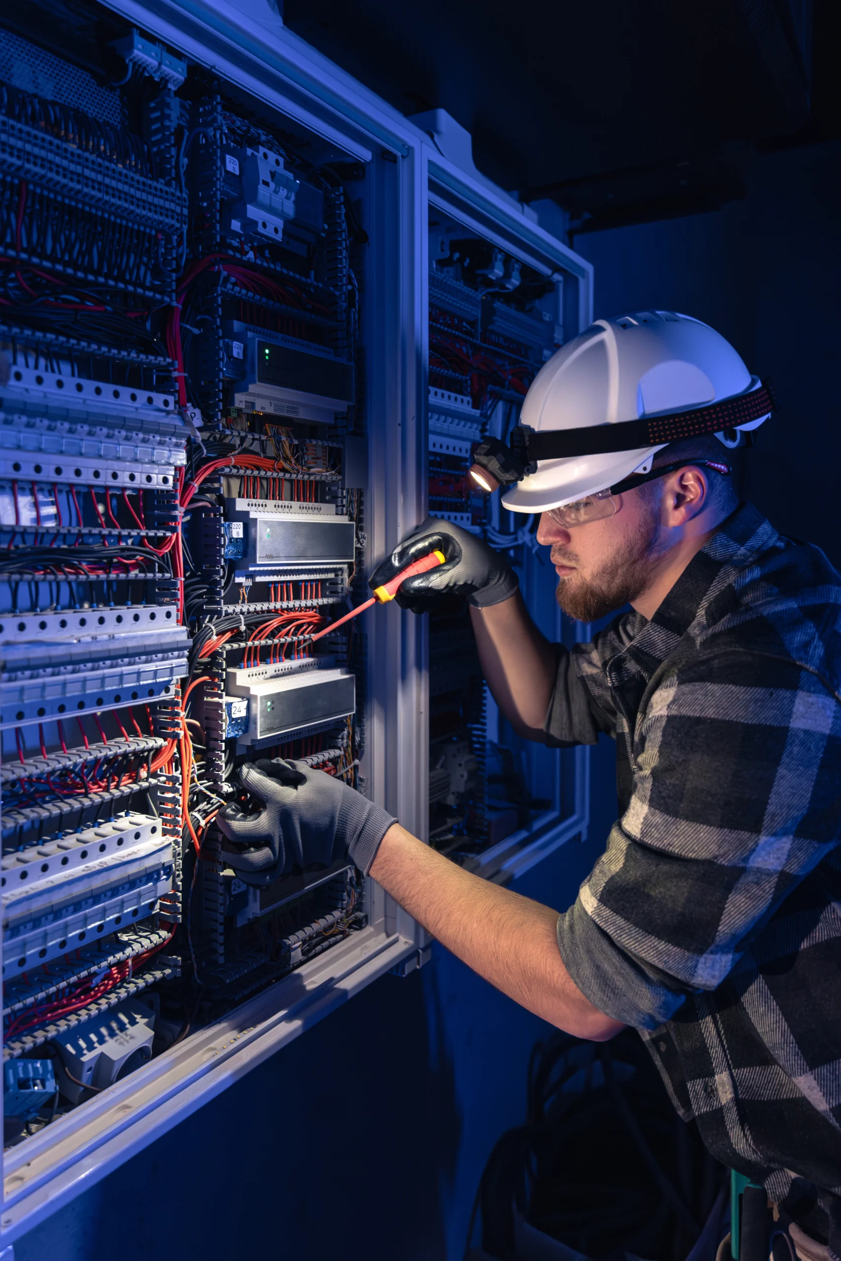 male electrician works switchboard overalls against backdrop emergency lighting